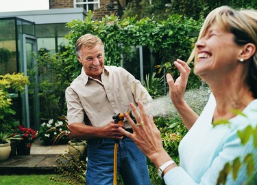 Mature Man Spraying a Woman With Water From His Garden Hose