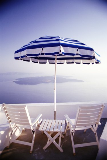 Rear view of wooden chairs and a table with umbrella on a balcony overlooking the ocean and the Greek Isles.