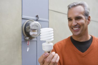 Man with home electric meter and compact fluorescent light bulb