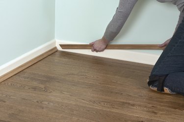 Man using hands to position edging bead at edge of laminate floor and skirting board