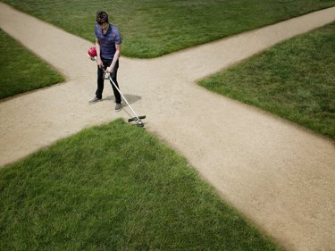 Man standing on dirt crossroad trimming lawn