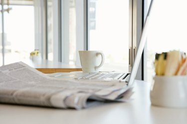 Newspaper by laptop computer in cafe