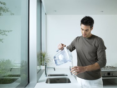 Man in kitchen pouring glass of filtered water