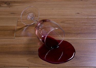 A wine glass spilling red wine on a hardwood floor