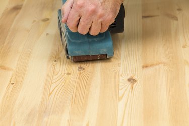 Mans hand on belt sander with pine wood