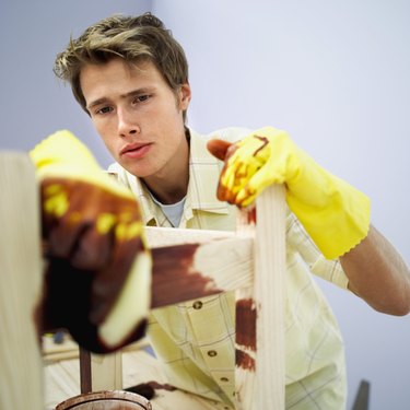 Young man applying wood varnish on a wooden chair with a paint brush