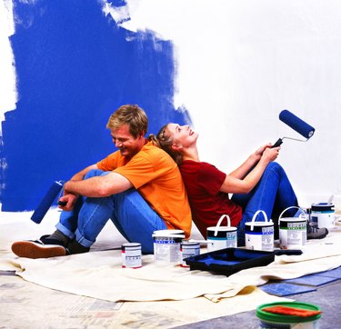 side profile of a couple sitting back to back with roller brushes of paint in hand