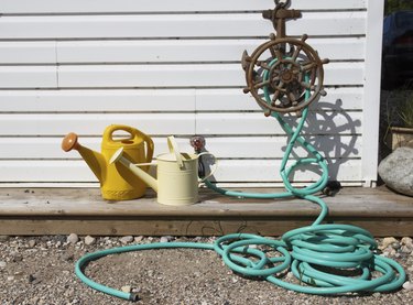 Green water hose and two watering cans outdoors