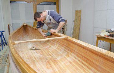 Young carpenter sanding new canoe in workshop