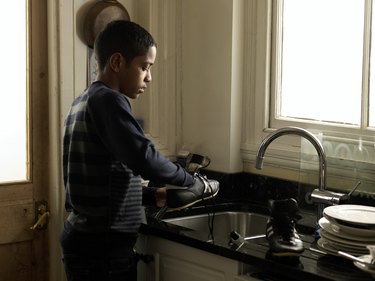 Boy (12-13) washing sport shoes in kitchen sink