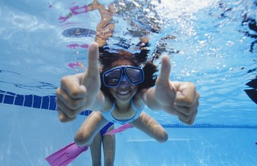 Girl (8-9) swimming underwater, showing thumbs up, underwater view