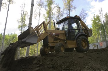 Yellow digger removing debris near forest, low angle view