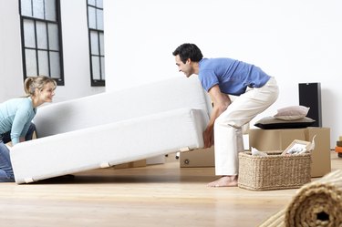 Couple lifting sofa, smiling, side view