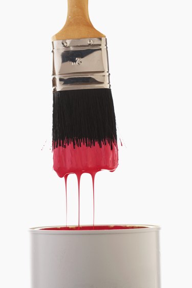 Paintbrush dripping red paint into paint can, close-up