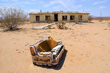 A torn up couch sits outside in front of a dilapidated building.