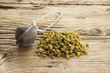 Dry camomile with tea strainer on old wooden table