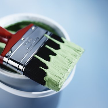 Paintbrush dipped in green paint resting on tin of paint