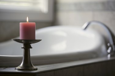 Pink candle burning beside bath tub in bathroom
