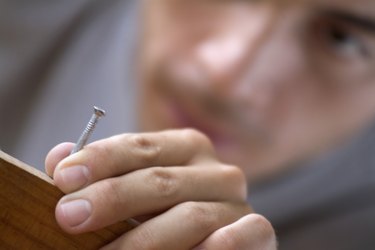 A Young man holding a nail in wood