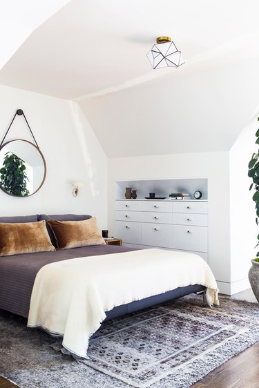 Midcentury bedroom with brown velvet throw pillows and circular mirror above the bed