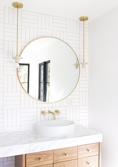 all-white midcentury bathroom with a round gold mirror and two hanging lighting fixtures