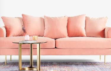 A blush-pink sofa in front of a round gold-legged side table.