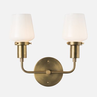 Brass wall sconce with two L-shaped lights featuring white shades