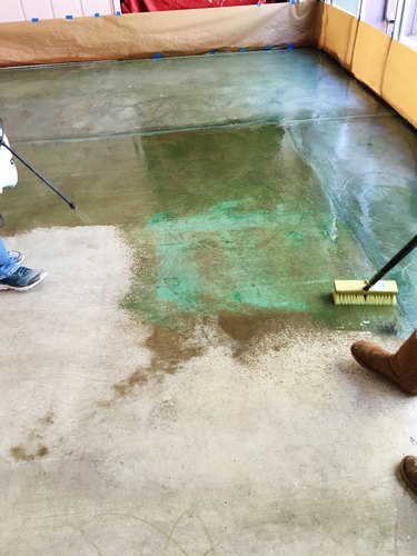 Person applying green acid stain to a concrete floor with a sprayer.