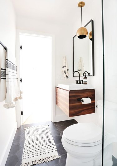 Modern bathroom with floating wood vanity, brass lamp, tile floors, toilet, towels and Scandinavian Bathroom Storage Ideas