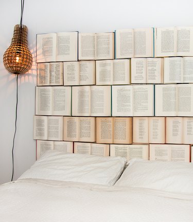 Opened books nailed to the wall serve as a headboard for a white bed.