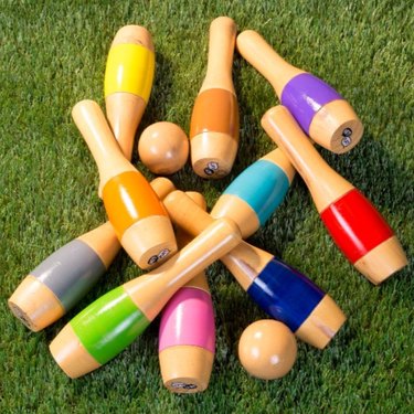 Colorful wooden bowling pins lay on a grass lawn.