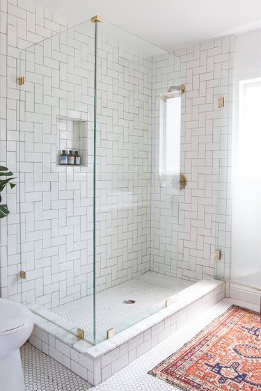 white midcentury bathroom tile with a colorful rug and frameless glass shower enclosure