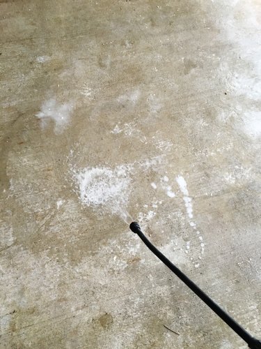 A pump sprayer spraying a concrete floor with water.