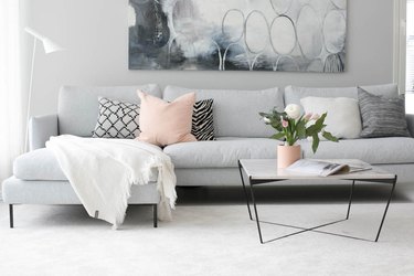 A gray couch, cream rug, and pink pillow.