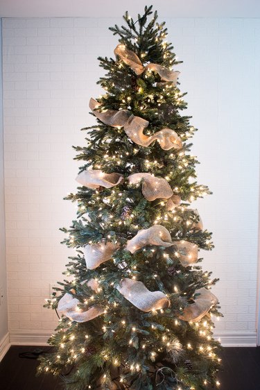 A Christmas tree has burlap ribbon from top to bottom