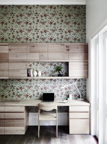 modern home office with floral wallpaper behind built-in desk and shelving