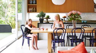 A woman and her daughter sitting at a blonde wood kitchen table in front of a waterfall-edge island with textured tile