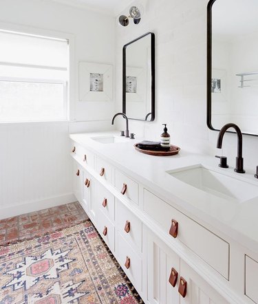 White bathroom with black faucets and tan leather drawer pulls
