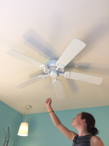 Woman using pull chain on ceiling fan