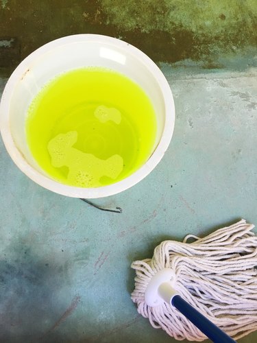 A bucket of neon yellow liquid next to a mop on a concrete floor.