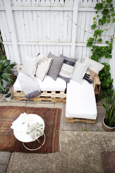 Wood pallet couch on patio with white cushions and throw pillows.