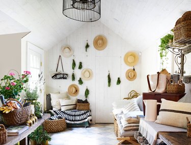 Hats and greenery hang on a white wall in an eclectic room