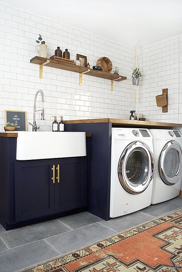 Laundry room with subway tile, navy blue cabinets and wood shelves.