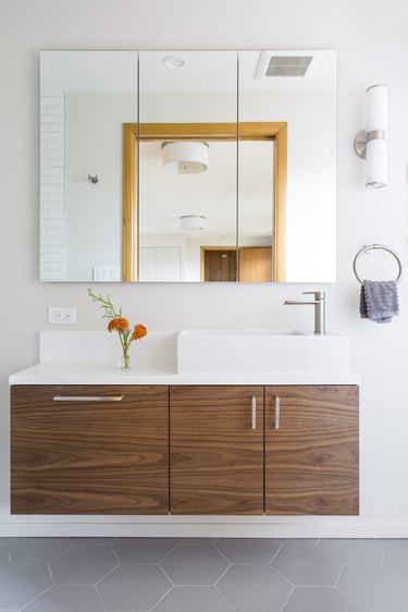 hexagonal midcentury bathroom tile idea in gray with frameless mirrors and wood vanity cabinet