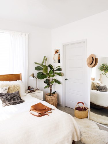 A white bedroom with a wood headboard, a large plant, and rattan baskets.