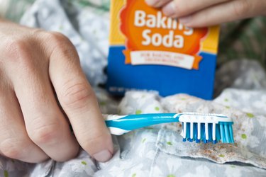 Hands holding baking soda and a toothbrush in front of fabric