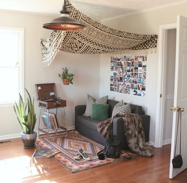 A black-and-white tapestry hangs over a gray couch and patterned rug