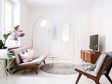 Ruang tamu berwarna putih dengan perabotan minimalis dan lampu lantai melengkung yang besar.