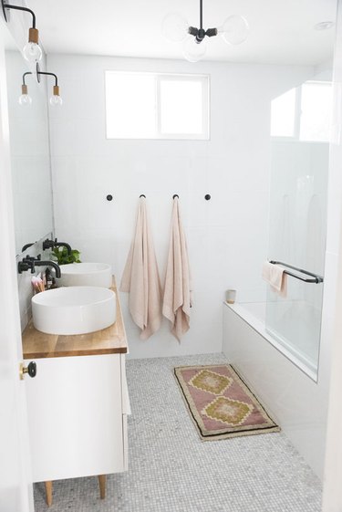 White bathroom with set of blush towels hanging on black pegs