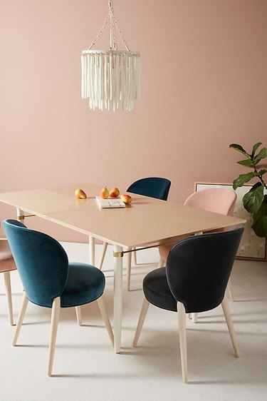 Four velvet dining chairs around a light-wood table with a pink wall.